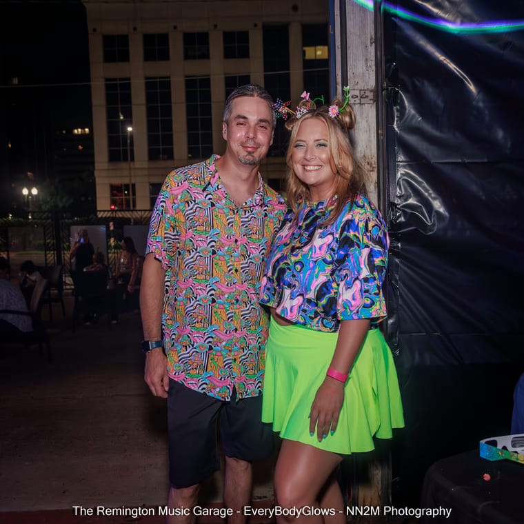 Two people smiling and wearing vibrant, colorful clothing at a night event