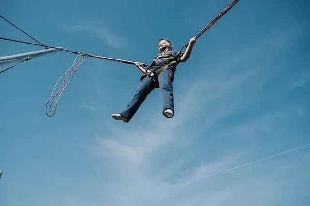 Child suspended on a bungee trampoline against a clear blue sky.