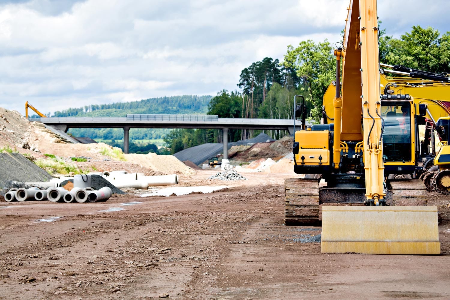 Excavator at a road construction site with concrete pipe sections